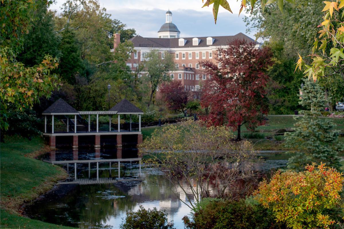 金沙全球赢家信心之选4066埃默里蒂公园, featuring fall foliage surrounding a small pond on campus, with a brick building in the background